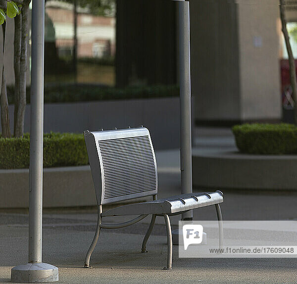 A silver metal bench sits between two poles in a city's urban park area; Vancouver  British Columbia  Canada