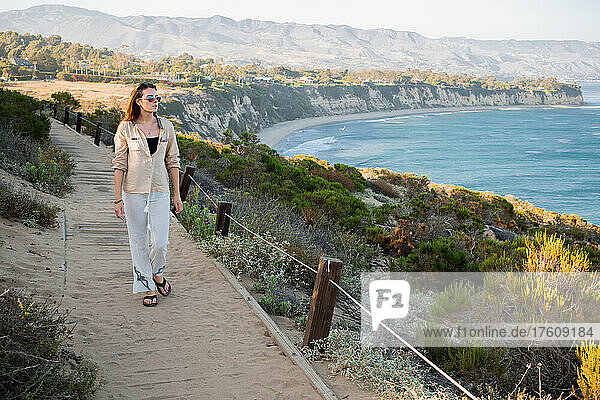 Eine junge Frau geht auf einem Pfad oberhalb des Strandes von Point Dume spazieren.