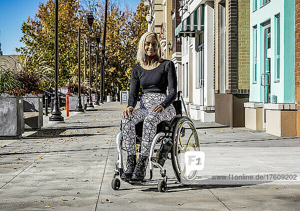 Außenporträt einer jungen querschnittsgelähmten Frau in ihrem Rollstuhl auf einem städtischen Gehweg an einem schönen Herbsttag; Edmonton  Alberta  Kanada