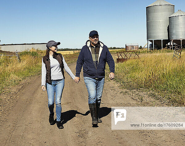 Älteres Paar  das sich an den Händen hält und einen unbefestigten Weg auf seiner Farm entlangläuft; Alcomdale  Alberta  Kanada