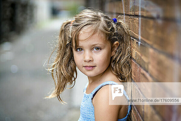 Outdoor portrait of a young girl standing against a brick wall in an alley; Toronto  Ontario  Canada