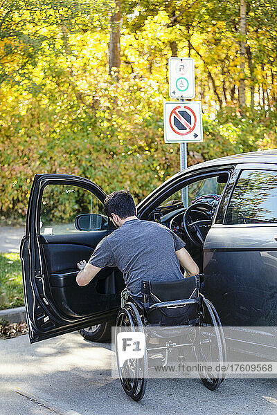Junger querschnittsgelähmter Mann setzt sich aus seinem Rollstuhl auf den Fahrersitz eines Autos; Edmonton  Alberta  Kanada