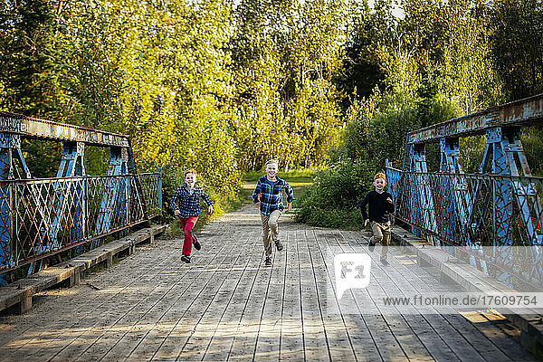 Three boys running across a bridge in a park in autumn; Edmonton  Alberta  Canada