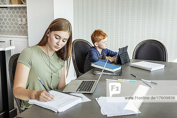 Ein Teenager und ein Junge sitzen zu Hause am Küchentisch mit einem Laptop und einem Tablet und machen Schularbeiten  während sie zu Hause unterrichtet werden; Alberta  Kanada