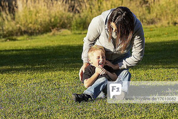 Mother and young son roughhousing on the grass in a city park; St. Albert  Alberta  Canada