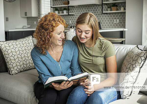 Mother and teenage daughter sitting on a couch at home reading the Bible together; Edmonton  Alberta  Canada