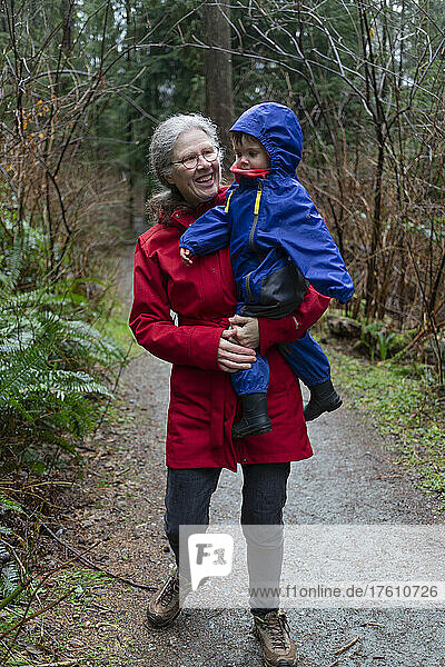 Großmutter hält ihre Enkelin im Vorschulalter im Arm  während sie einen Waldweg entlanglaufen; North Vancouver  British Columbia  Kanada