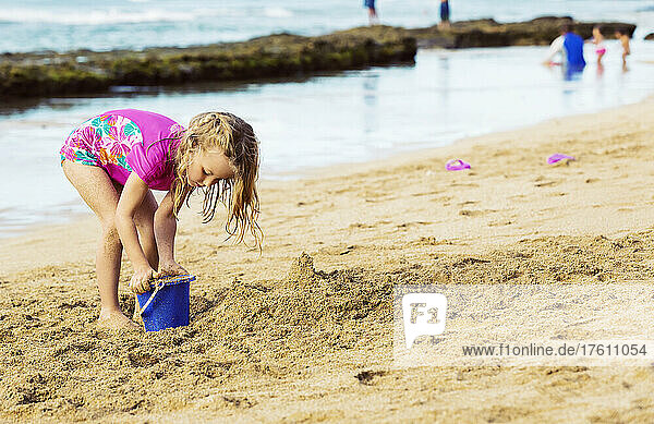 A young girl playing in the sand with a pail on a beach at Ka'anapali; Ka'anapali  Maui  Hawaii  United States of America