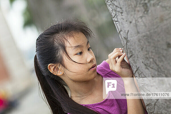 Porträt eines Mädchens im Freien  das das Detail einer Baumrinde betrachtet; Hongkong  China