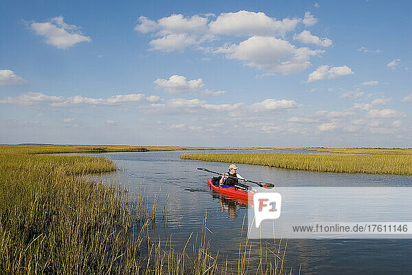 A sea kayaker and fisherman paddles through a salt water marsh.; Core Banks  North Carolina.