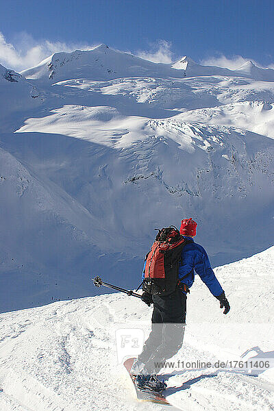 A back country snowboarder descends a snow field toward a glacier.; Selkirk Mountains  British Columbia  Canada.