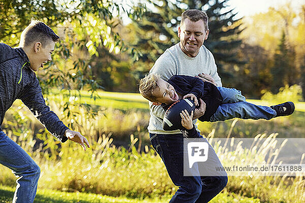 Father playing with his two sons in a park in autumn; St. Albert  Alberta  Canada