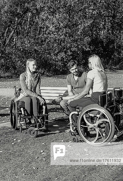 Black and white image of a group of three young paraplegics in their wheelchairs visiting together in a park on a beautiful sunny day; Edmonton  Alberta  Canada