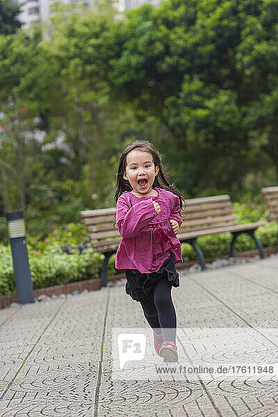 Junges Mädchen läuft im Freien in einem Stadtpark auf die Kamera zu; Hongkong  China