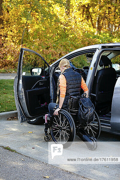 Junge querschnittsgelähmte Frau bewegt sich von ihrem Rollstuhl zum Fahrersitz eines Autos auf einem Parkplatz; Edmonton  Alberta  Kanada