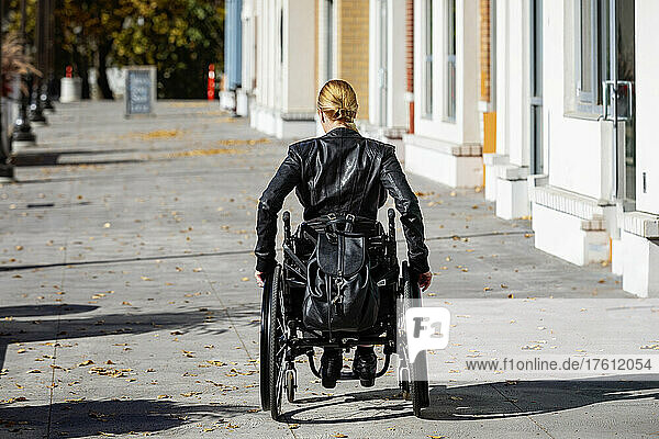 Junge querschnittsgelähmte Frau in ihrem Rollstuhl  die an einem schönen Herbsttag einen städtischen Gehweg hinunterfährt; Edmonton  Alberta  Kanada