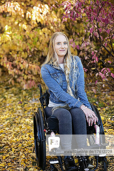 Eine junge querschnittsgelähmte Frau in ihrem Rollstuhl in einem Park an einem schönen Herbsttag; Edmonton  Alberta  Kanada