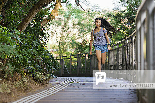 Young girl with long hair running down an outdoor park path and looking at the camera; Hong Kong  China