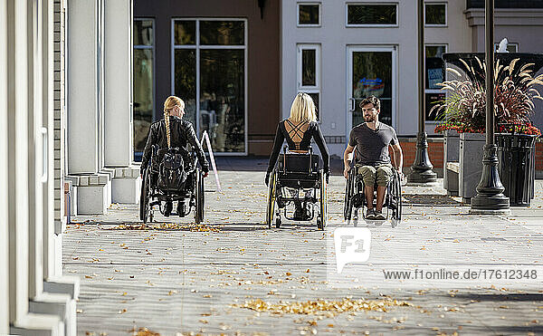 Three young paraplegic friends spending time together moving down a walkway outside in a city area; Edmonton  Alberta  Canada