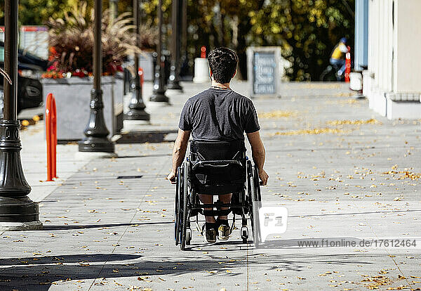 Young paraplegic man in his wheelchair going down a city walkway on a beautiful fall day; Edmonton  Alberta  Canada