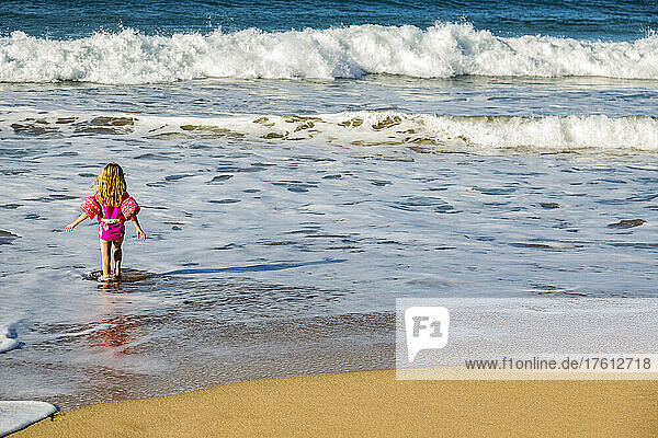 Blick von hinten auf ein junges Mädchen  das vom Strand ins Wasser geht  während die Wellen an das Ufer von D.T. Fleming rollen; Kapalua  Maui  Hawaii  Vereinigte Staaten von Amerika