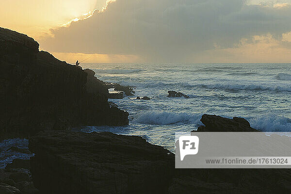 Silhouette of man surf fishing along a rugged coastline at sunset; Praia do Guincho  Cascais  Portugal