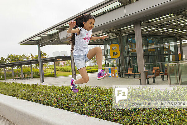 Mädchen  das auf einem Gehweg am Kai Tak Cruise Terminal in die Luft springt; Hongkong  China