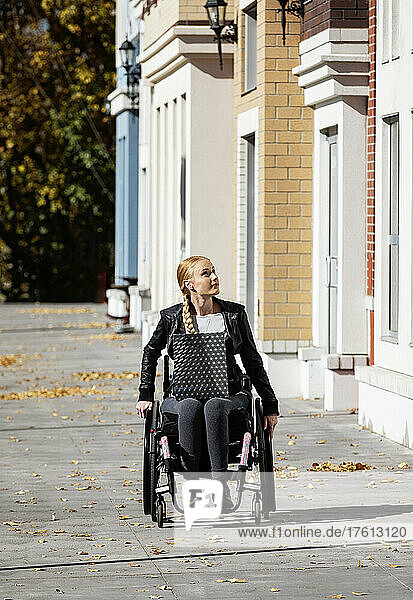 Junge querschnittsgelähmte Frau in ihrem Rollstuhl mit einer Einkaufstasche  die an einem schönen Herbsttag einen städtischen Gehweg hinunterfährt; Edmonton  Alberta  Kanada