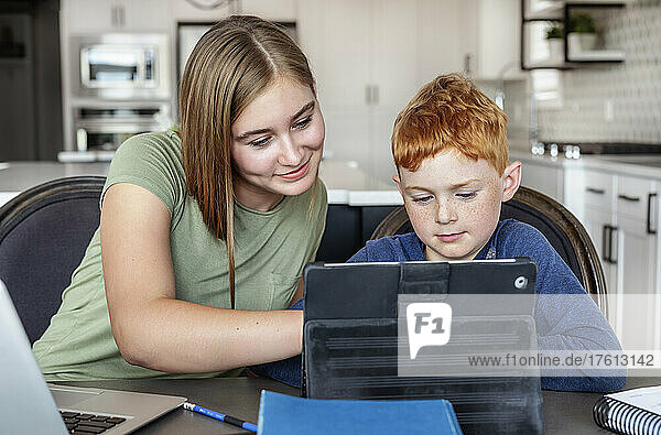 Ein Teenager und ein Junge sitzen zu Hause am Küchentisch mit einem Laptop und einem Tablet und machen Schularbeiten  während sie zu Hause unterrichtet werden; Alberta  Kanada