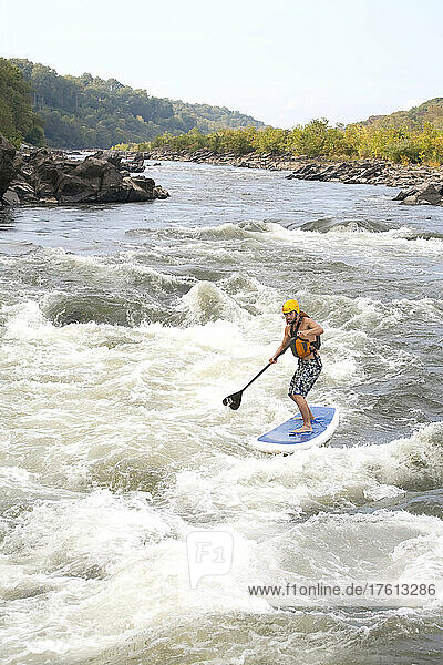 Ein Mann auf einem Stand Up Paddle Board fährt auf dem Potomac River durch Stromschnellen; Bethesda  Maryland.