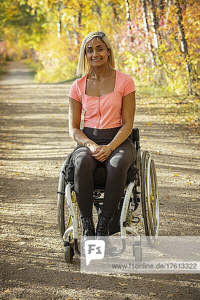 Porträt einer jungen querschnittsgelähmten Frau in ihrem Rollstuhl auf einem Weg in einem Park an einem schönen Herbsttag; Edmonton  Alberta  Kanada