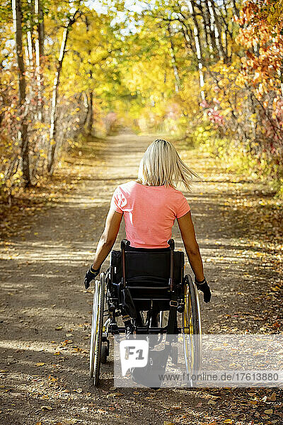 Young paraplegic woman in her wheelchair going down a trail in a park on a beautiful fall day; Edmonton  Alberta  Canada