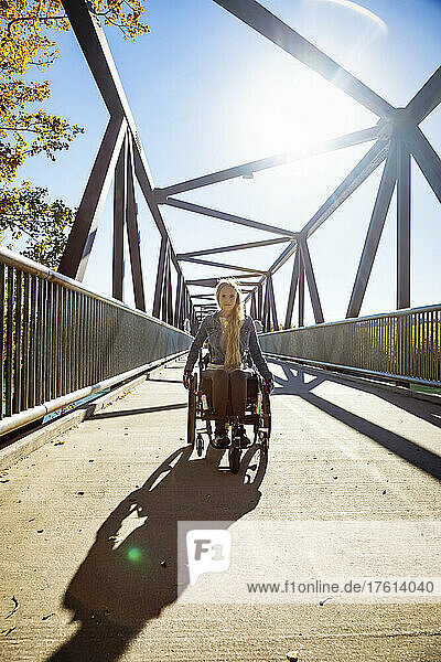 Eine junge querschnittsgelähmte Frau  die an einem schönen Herbsttag in ihrem Rollstuhl über eine Brücke fährt; Edmonton  Alberta  Kanada