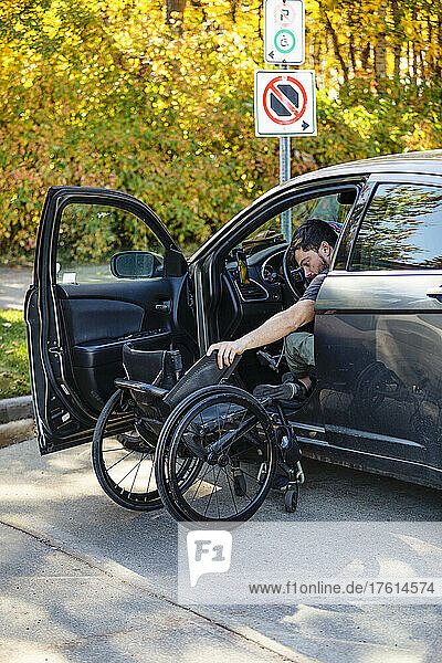 Junger querschnittsgelähmter Mann setzt sich aus seinem Rollstuhl auf den Fahrersitz eines Autos; Edmonton  Alberta  Kanada