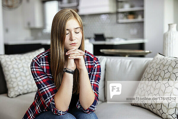 Teenage girl sitting on a couch at home and spending time in prayer; Edmonton  Alberta  Canada