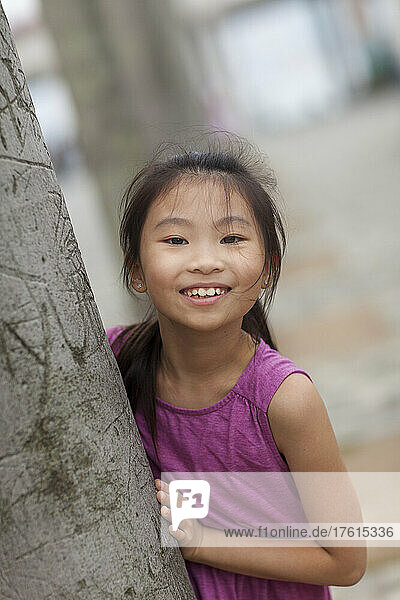 Porträt eines Mädchens im Freien  das hinter einem Baum steht; Hongkong  China