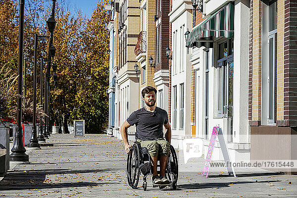 Young paraplegic man in his wheelchair going down a city walkway on a beautiful fall day; Edmonton  Alberta  Canada