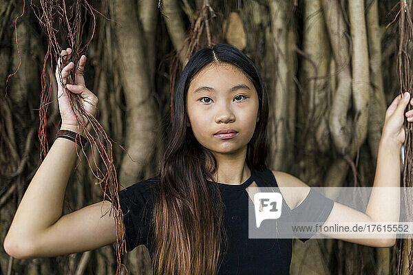 Porträt eines Mädchens im Teenageralter  das zwischen Weinreben und Baumwurzeln steht; Hongkong  China