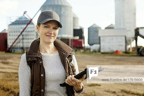 Porträt einer reifen Frau  die auf ihrer Farm arbeitet  einen Tablet-Computer in der Hand hält und vor einer Getreidemühle steht; Alcomdale  Alberta  Kanada