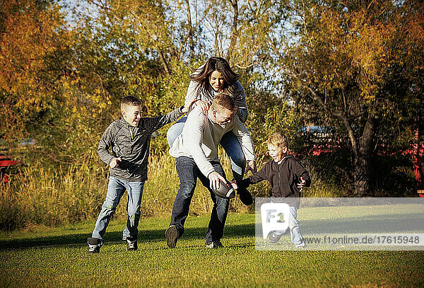 A young family with two boys plays football in a city park in autumn; St. Albert  Alberta  Canada