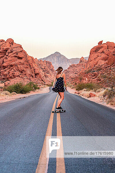 A woman skateboards down an empty desert road.