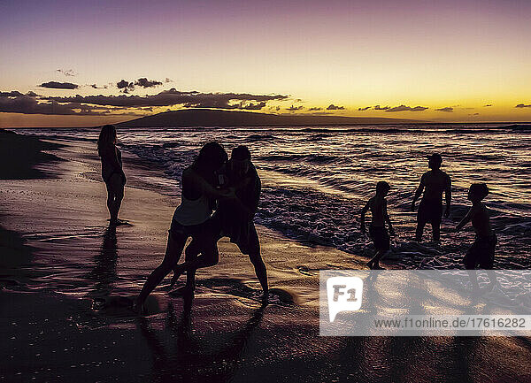Silhouette von Touristen  die am nassen Strand des Ka'anapali Beach Resort spielen  mit einem dramatischen  farbenfrohen Sonnenuntergang am Horizont mit der Insel Lanai in der Ferne; Ka'anapali  Maui  Hawaii  Vereinigte Staaten von Amerika