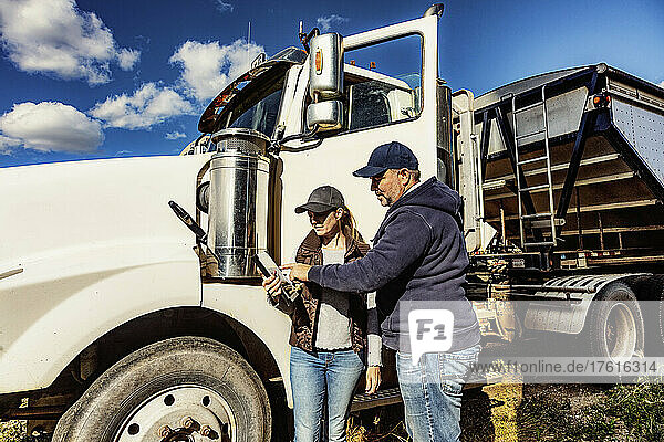 Mature couple working on their farm  standing next to a diesel transport truck and consulting their tablet computer; Alcomdale  Alberta  Canada
