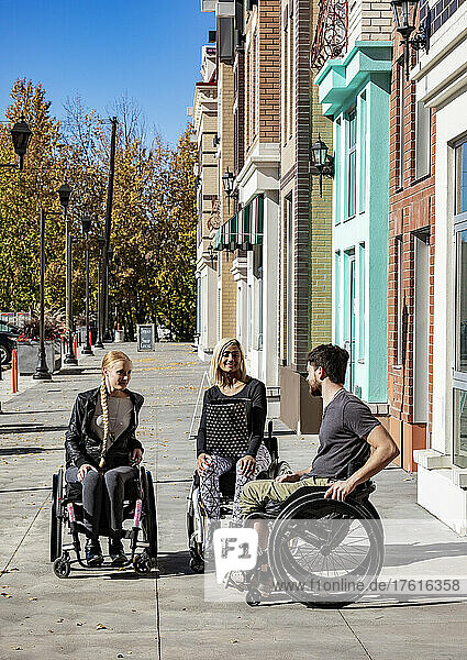 Junge Querschnittsgelähmte in ihren Rollstühlen besuchen an einem schönen Herbsttag gemeinsam einen Gehweg  einer hält eine Einkaufstasche; Edmonton  Alberta  Kanada