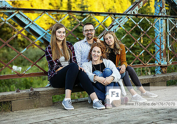 Außenporträt von Eltern mit zwei Töchtern im Teenageralter  die auf einer Brücke in einem Stadtpark im Herbst sitzen; Edmonton  Alberta  Kanada