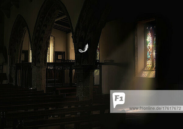 Eine weiße Feder schwebt von der Decke einer Kirche herab  während das Sonnenlicht durch ein Buntglasfenster scheint; Richmond  North Yorkshire  England
