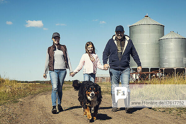Eltern und ihre kleine Tochter gehen auf einem unbefestigten Weg mit ihrem Hund auf ihrer Familienfarm spazieren; Alcomdale  Alberta  Kanada