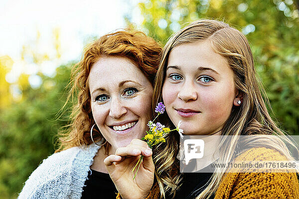 Outdoor portrait of a mother with her teenage girl holding a small cluster of colourful wildflowers and looking at the camera; Edmonton  Alberta  Canada