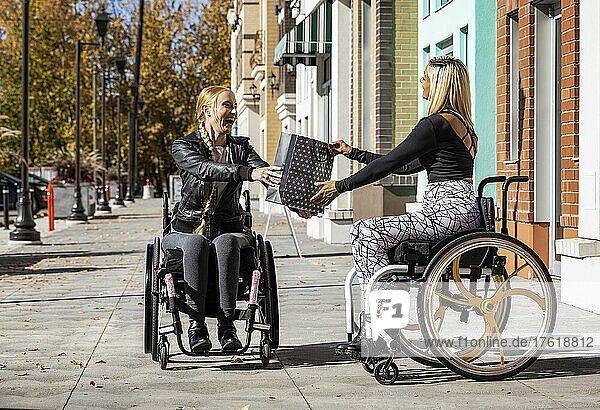 Zwei junge  querschnittsgelähmte Frauen in ihren Rollstühlen besuchen an einem schönen Herbsttag gemeinsam einen Gehweg  wobei die eine der anderen ein Geschenk überreicht; Edmonton  Alberta  Kanada