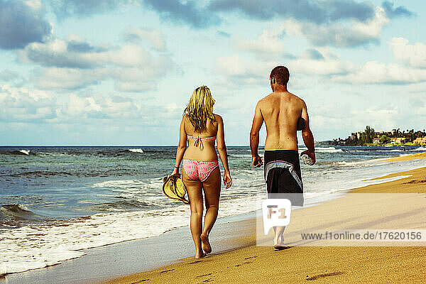 A couple walks down Ka'anapali beach at the water's edge wearing swimwear; Ka'anapali  Maui  Hawaii  United States of America
